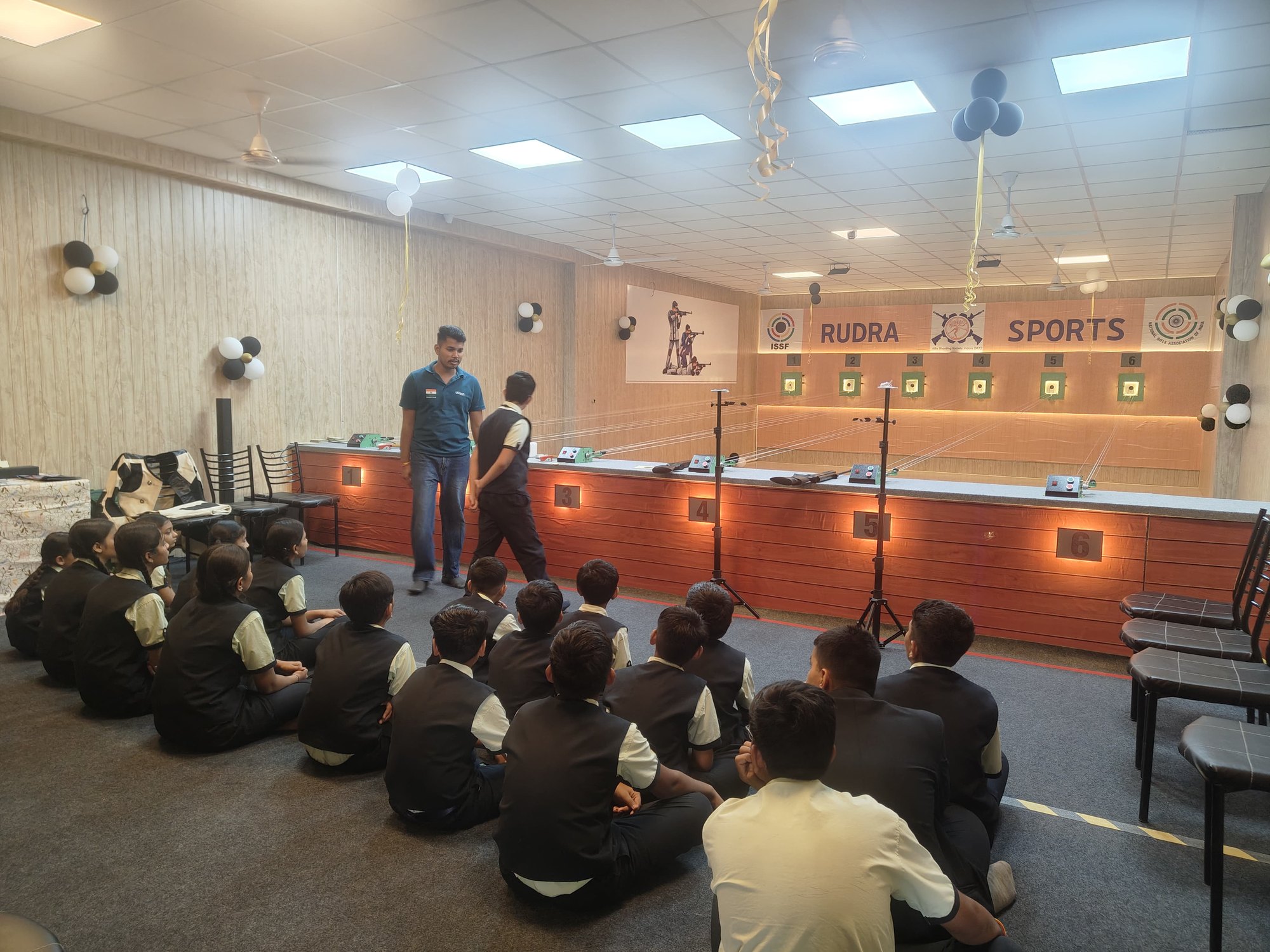 School students seated on the floor listening to a coach in front of the firing line
