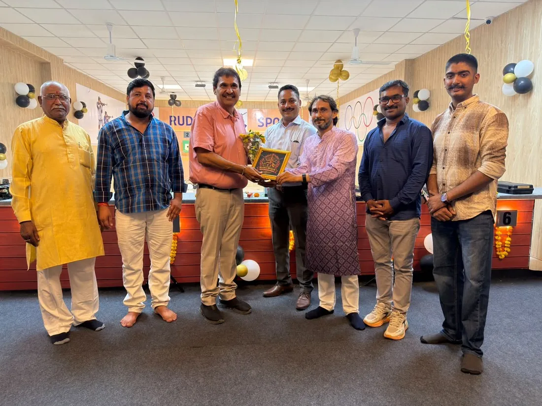 Seven guests standing together as a memento is presented in front of the Rudra Sports banner