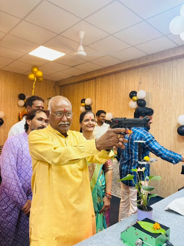 A guest in a yellow kurta aiming an air pistol during the inauguration, with other guests watching
