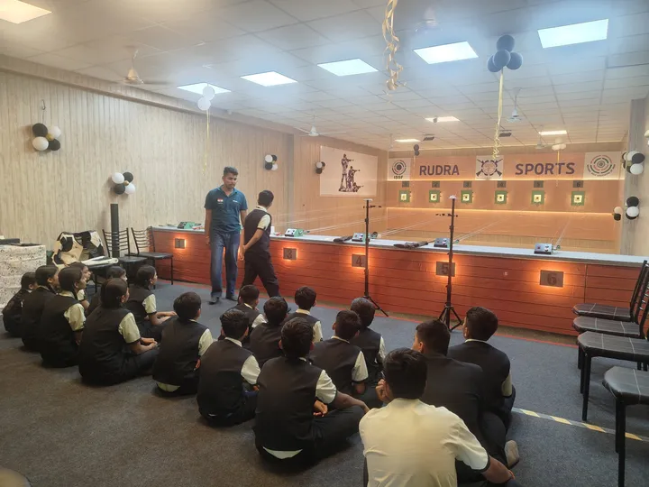 School students seated on the floor listening to a coach in front of the firing line